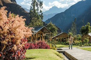 Un resort con cabañas de madera, un camino pavimentado y montañas al fondo.