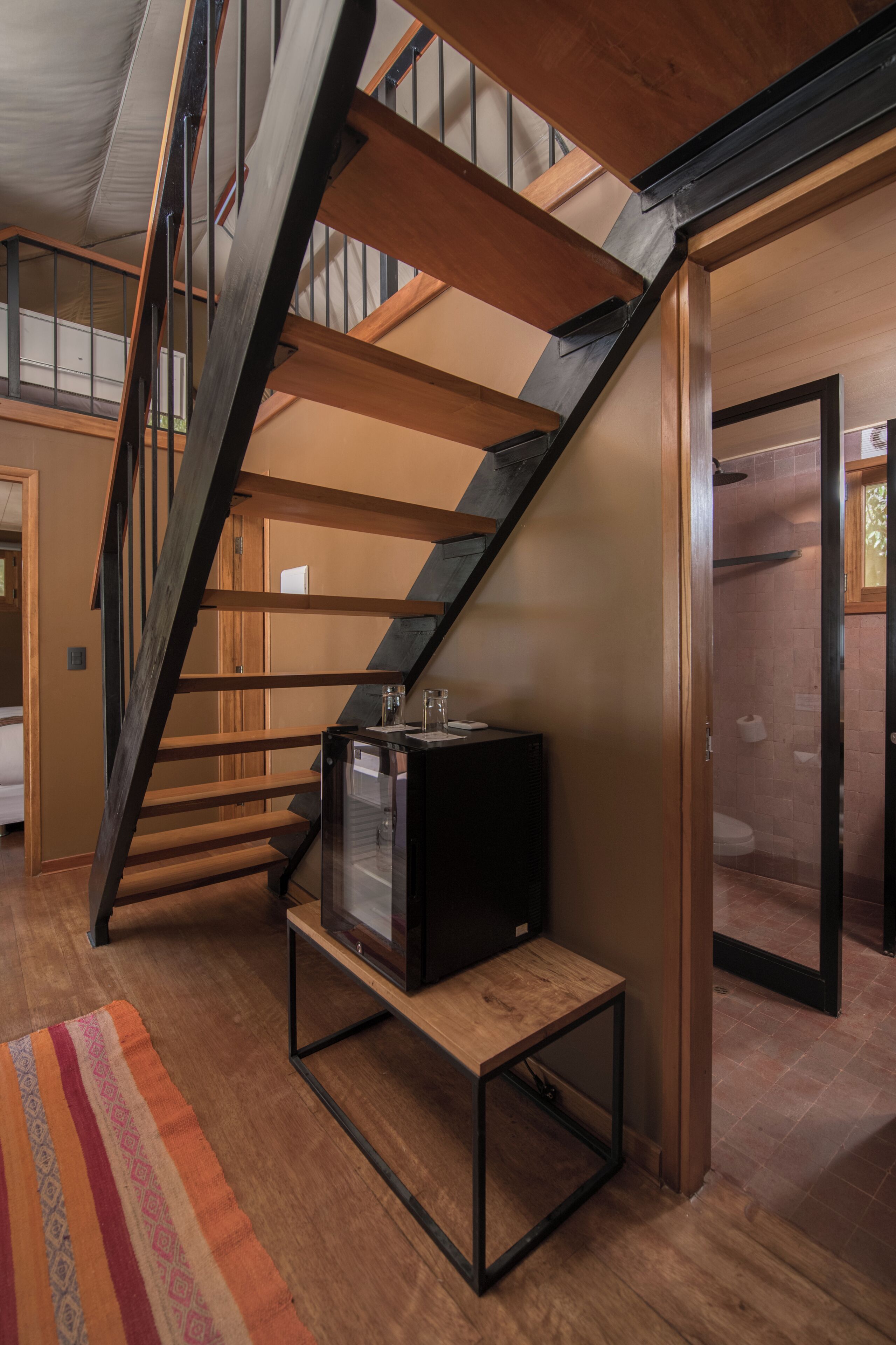 A modern staircase with wooden steps and metal railings, leading to an upper floor. A small table with a television is placed on the lower landing.