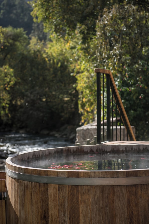Een hottub met houten buitenkant, omringd door weelderige begroeiing en een stenen constructie.