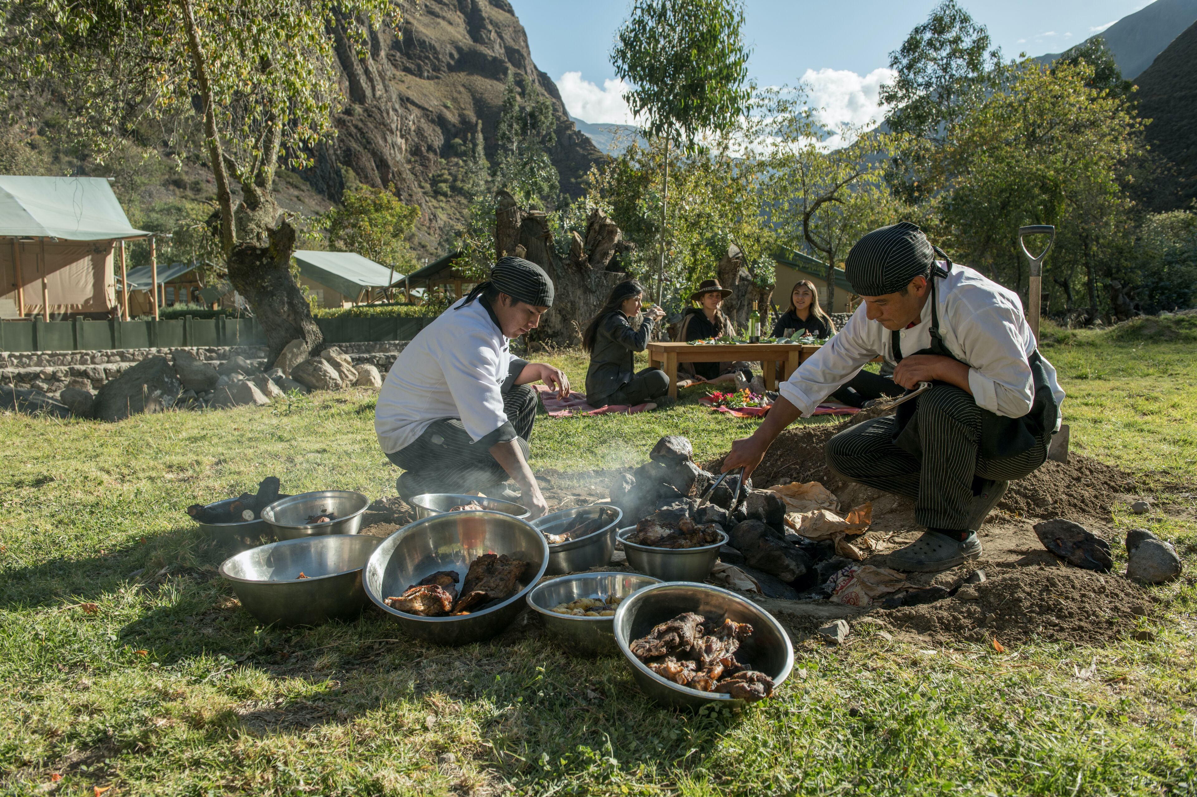 Un grupo de personas cocinando al aire libre usando ollas de metal y fuego.