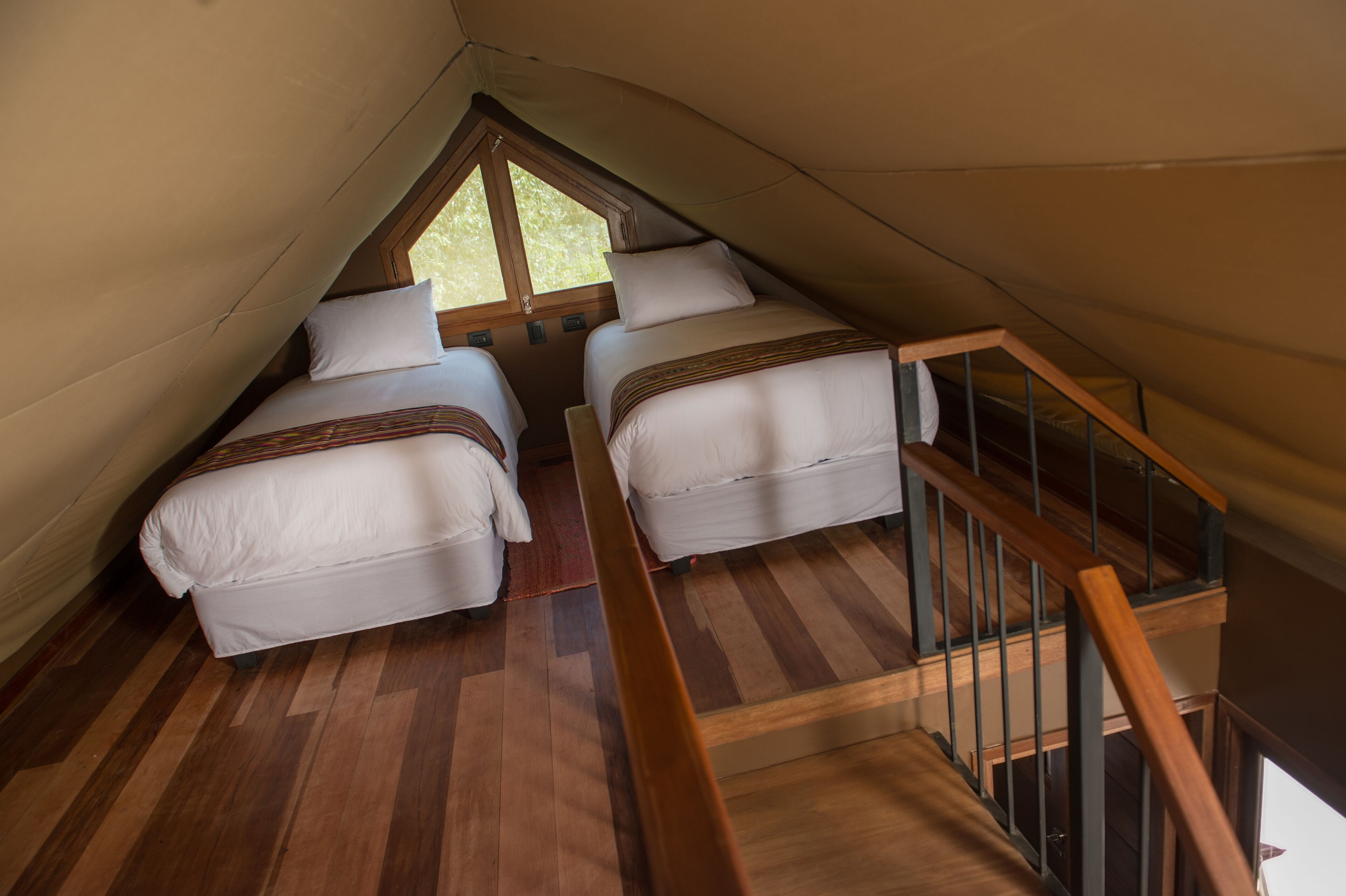 A bedroom with two beds, wooden flooring, a wooden staircase, and a window.