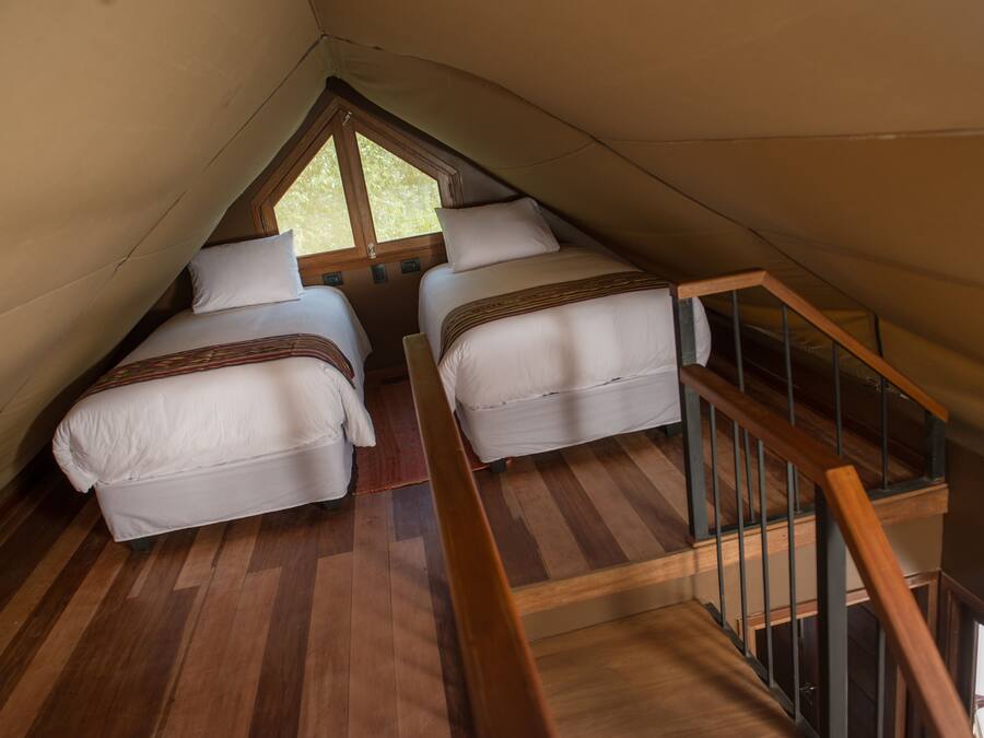 A bedroom with two beds, wooden flooring, a wooden staircase, and a window.