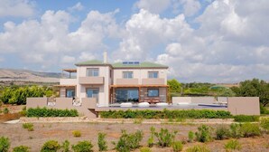A two-story modern house with a flat roof, large windows, and a covered outdoor seating area.
