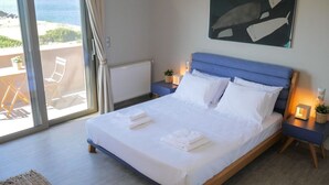 A bedroom with a bed, a nightstand, a lamp, and a view of the ocean.