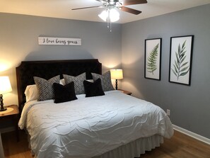 A neatly made bed with patterned pillows, a bedside lamp, and a wall sign.