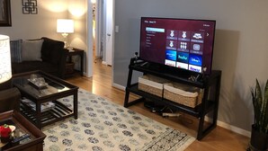 Una sala de estar con un televisor de pantalla plana sobre un mueble bajo, un sofá, una mesa de centro y una alfombra estampada.
