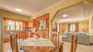 A spacious living area with a dining table set for four, a kitchen with wooden cabinets, and a grey sofa in the background.