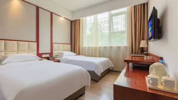 A hotel room with two beds, a desk with a lamp, a television, and a window with curtains.