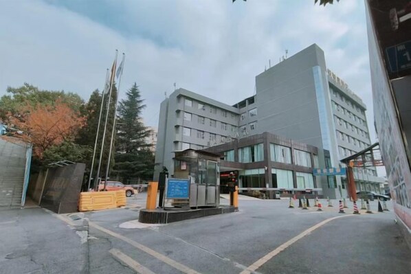 A modern building with a central entrance, a small kiosk, and a parking area with yellow barriers.