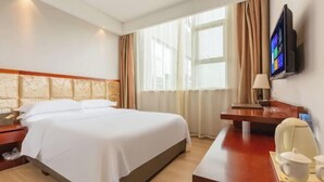 Habitación de hotel con cama, escritorio con silla, televisor y ventana con cortinas.