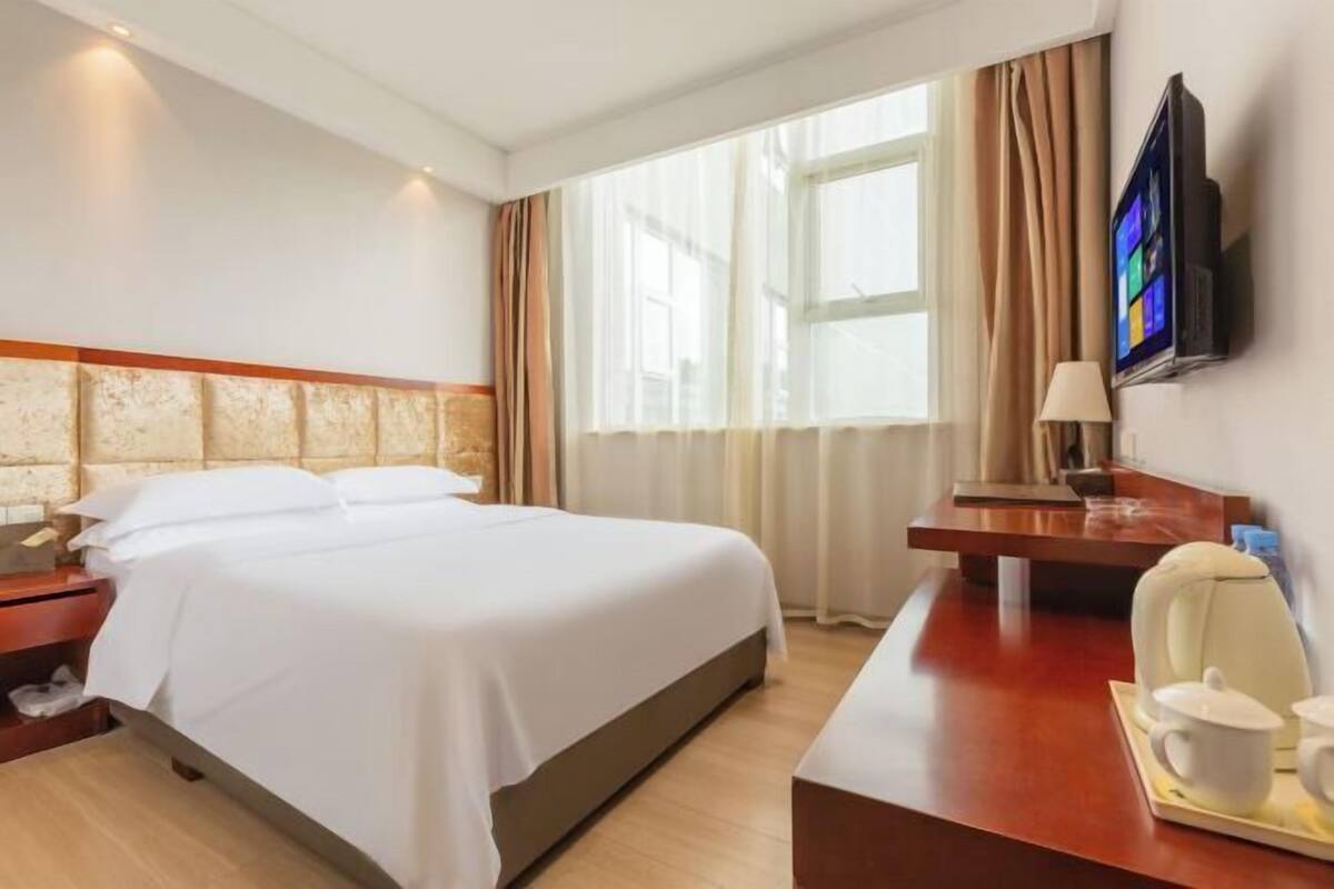 Ein Hotelzimmer mit einem Bett, einem Schreibtisch mit Stuhl, einem Fernseher und einem Fenster mit Vorhängen.
