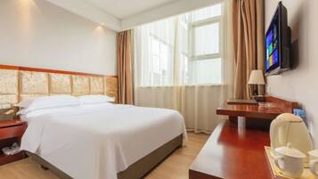 A hotel room with a bed, a desk with a chair, a TV, and a window with curtains.