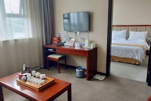 A hotel room with a bed, a desk with a TV, a table with teaware, and a window with curtains. - Joy Opulence Hotel (Guiyang)