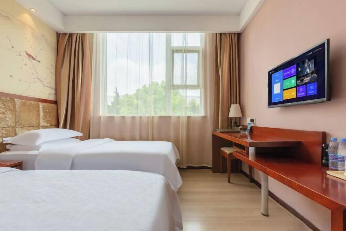 Ein Hotelzimmer mit zwei Betten, einem Schreibtisch, einem Fernseher und einem fenster mit Vorhängen.