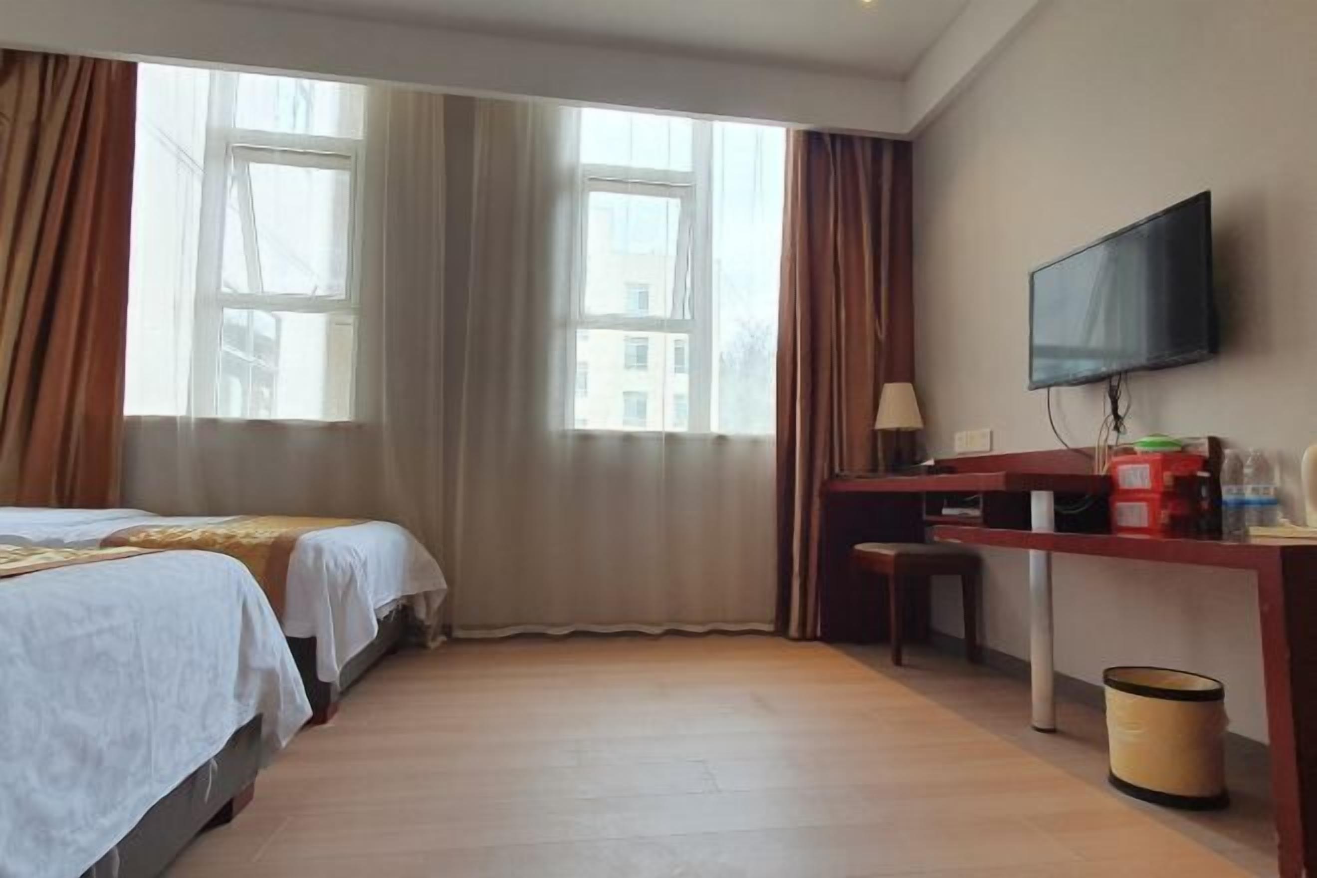 Habitación de hotel con dos camas, un escritorio, un televisor y una ventana con cortinas.