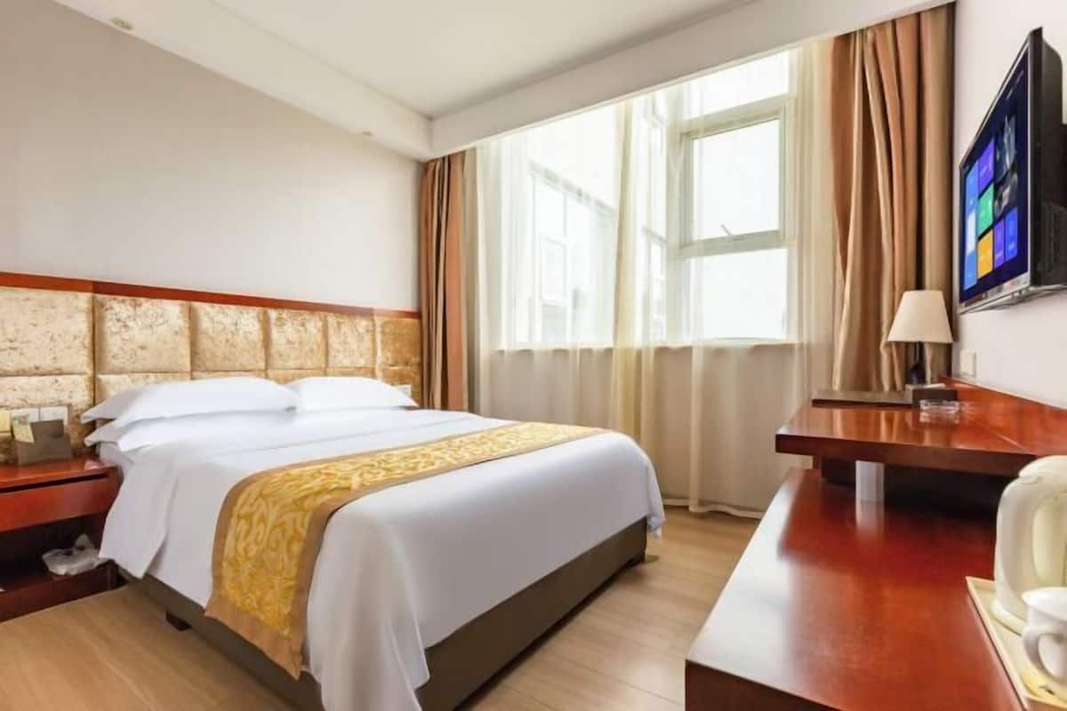 Ein Hotelzimmer mit Bett, Schreibtisch, Fernseher und einem Fenster mit Vorhängen.