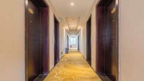 A hotel hallway with a carpeted floor, doors on both sides, and a light source at the end.