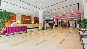 A spacious lobby with a reception desk, a purple table, and potted plants.