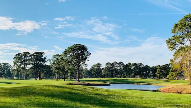 Campo de golf con un estanque, árboles y cielo despejado.
