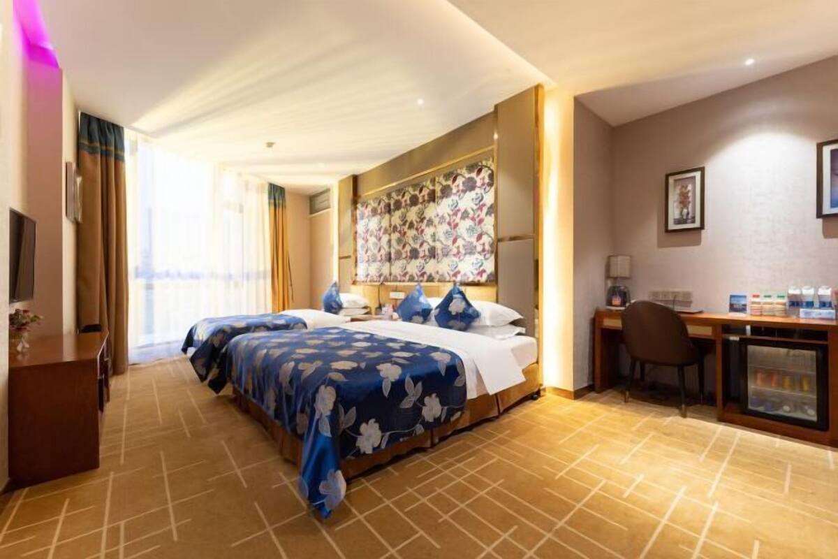 A hotel room with a large bed, a desk, a chair, and a minibar.