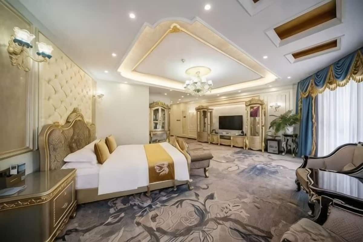 A luxurious hotel room with a large bed, a television, a seating area, and a decorative ceiling.