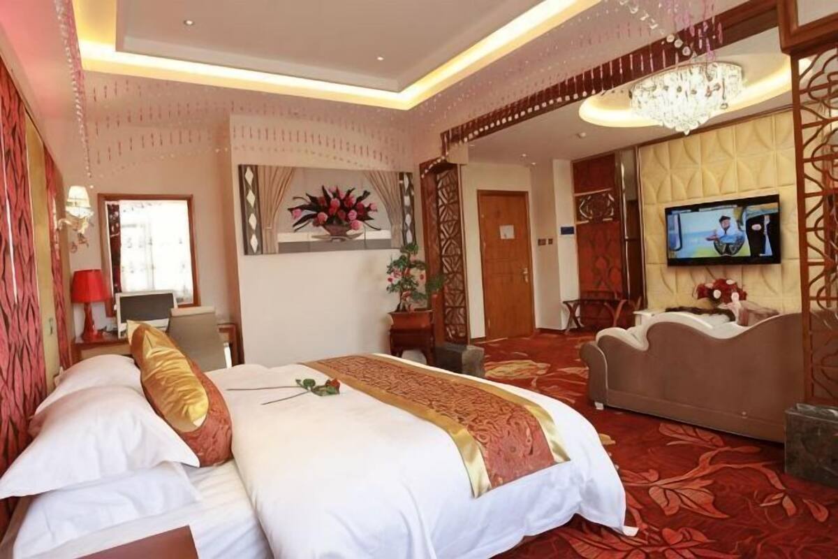 A hotel room with a large bed, a television, a sofa, and a decorative wall.