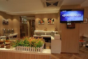 A hotel lobby with a reception desk, a television screen, and a decorative plant.