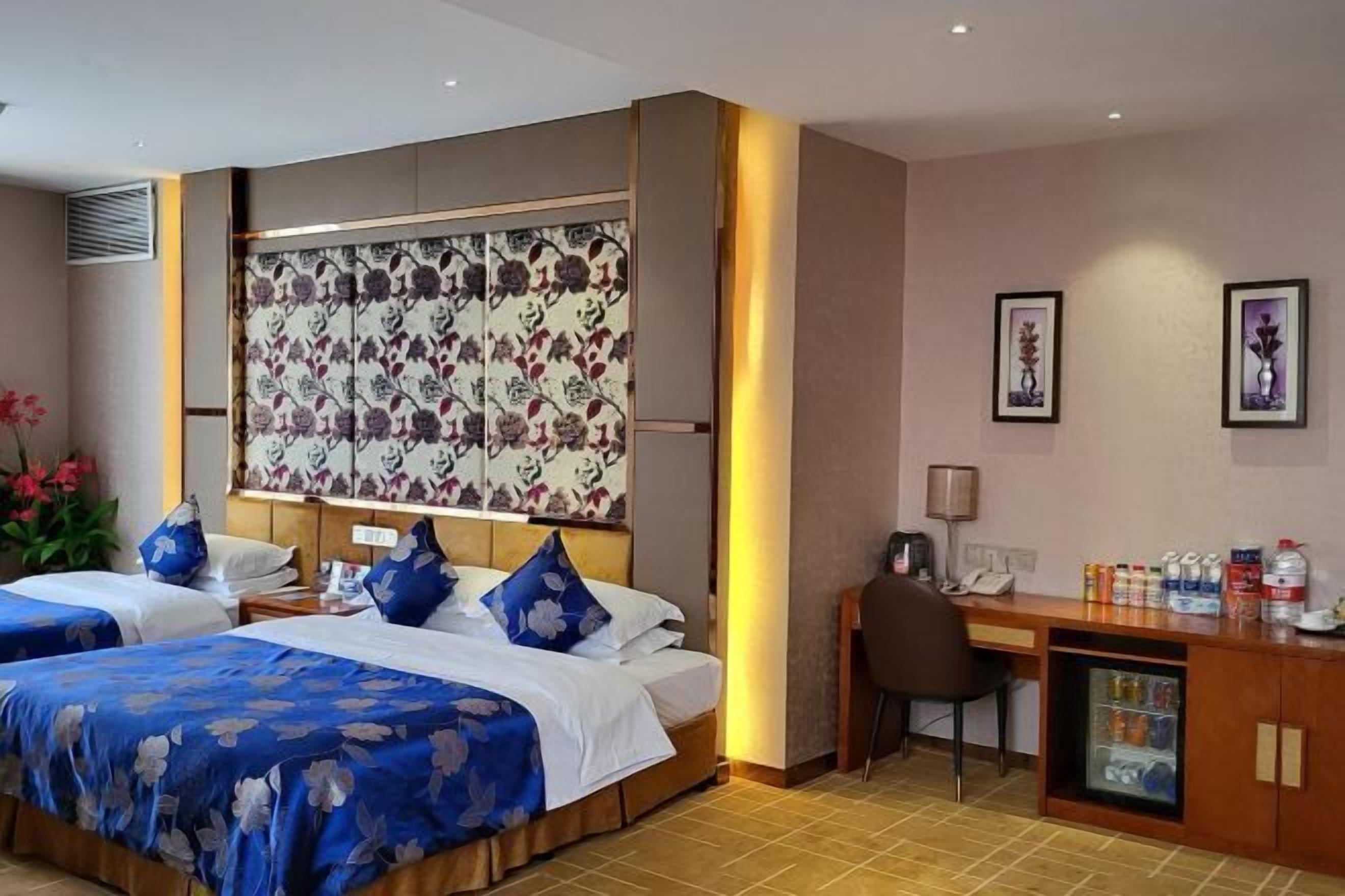 A hotel room with two beds, a desk, a chair, a minibar, and a large floral-patterned partition.