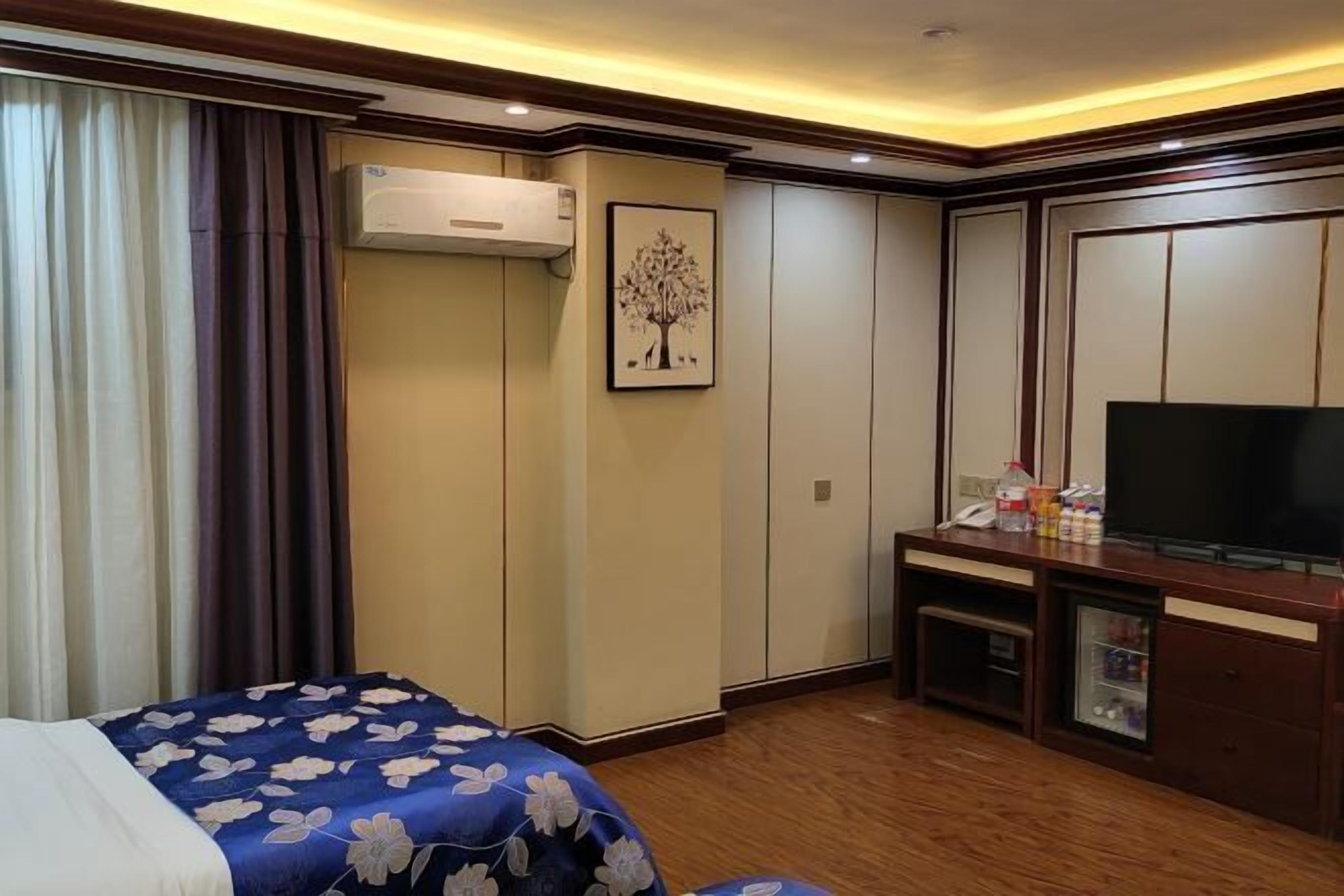 A hotel room with a bed, a TV, a desk with a computer, and a wardrobe.