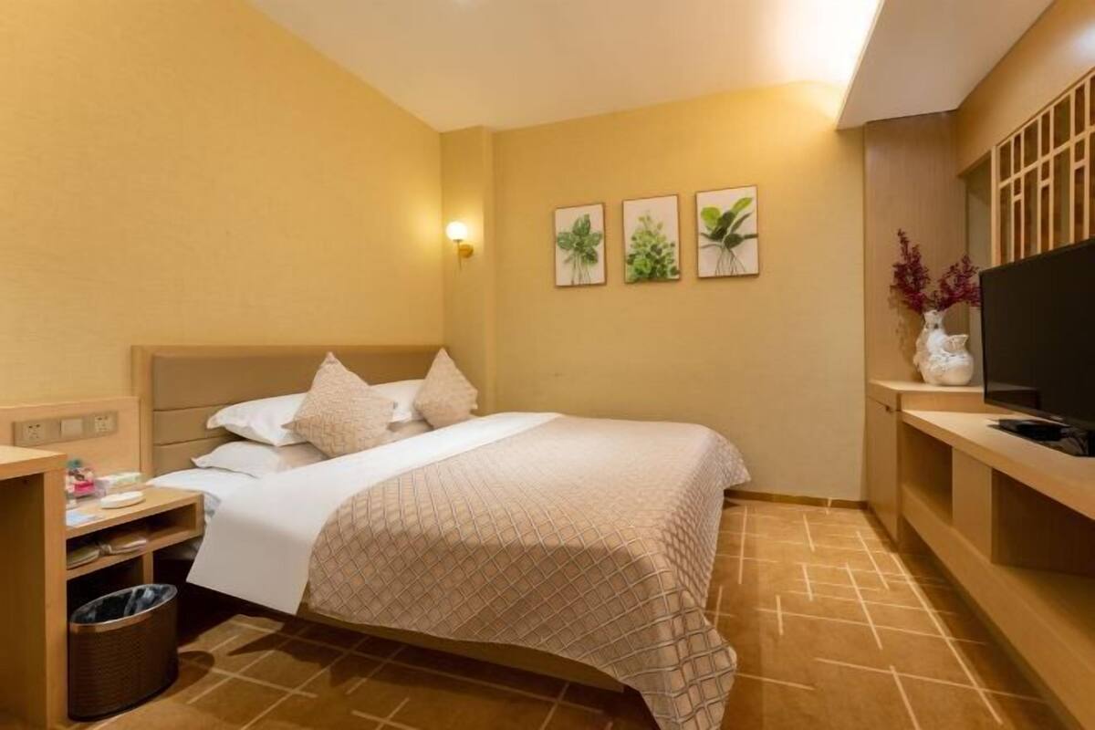 A hotel room with a bed, a TV, a small desk, and a trash bin.