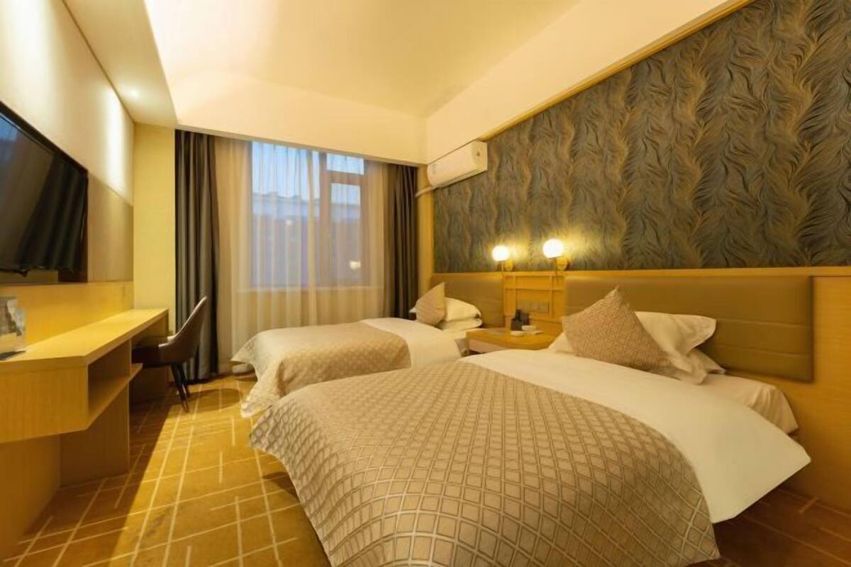 A hotel room with two beds, a desk, a TV, and a window with curtains.