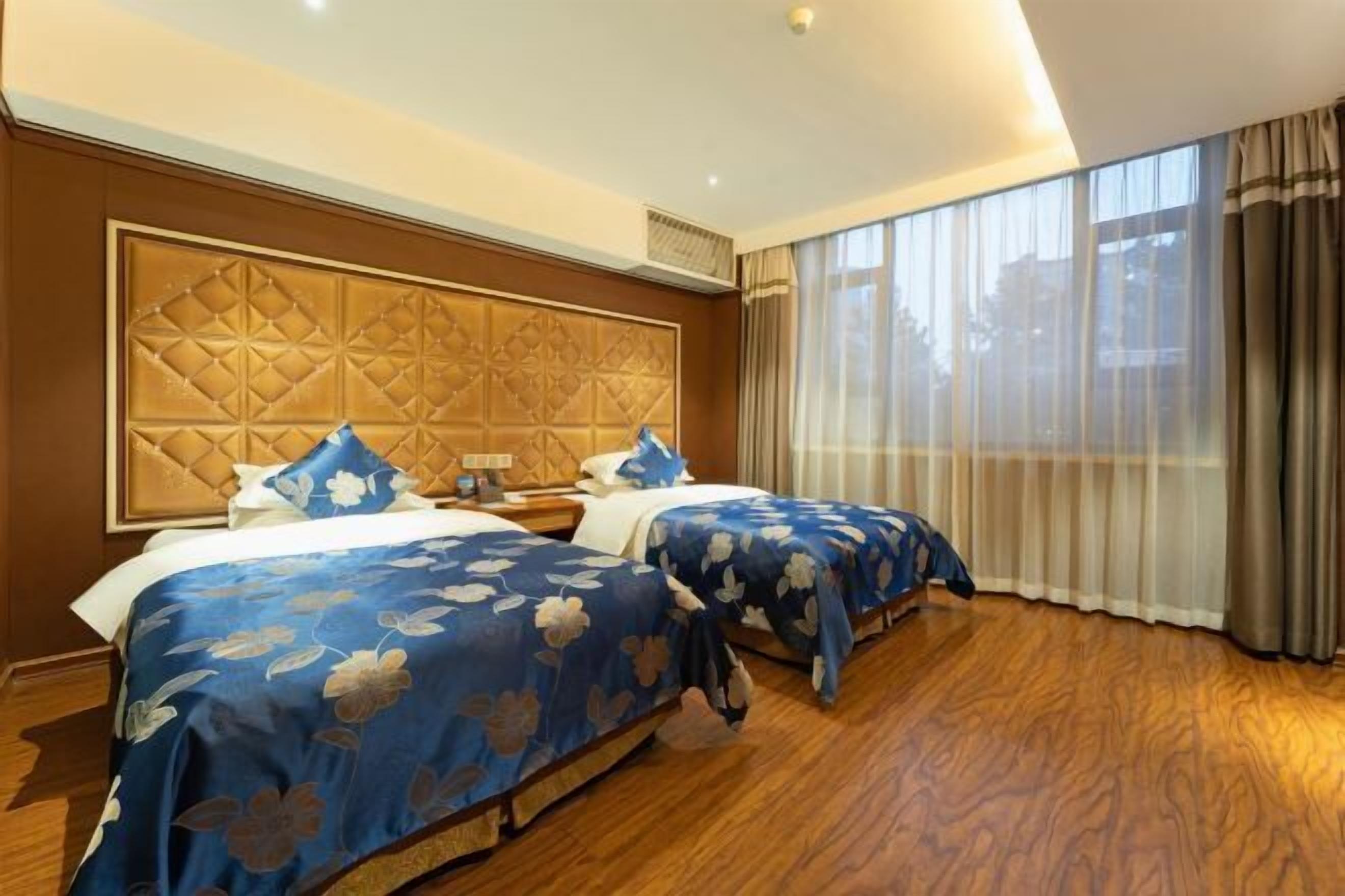 A hotel room with two beds, a large window with curtains, and a wooden floor.