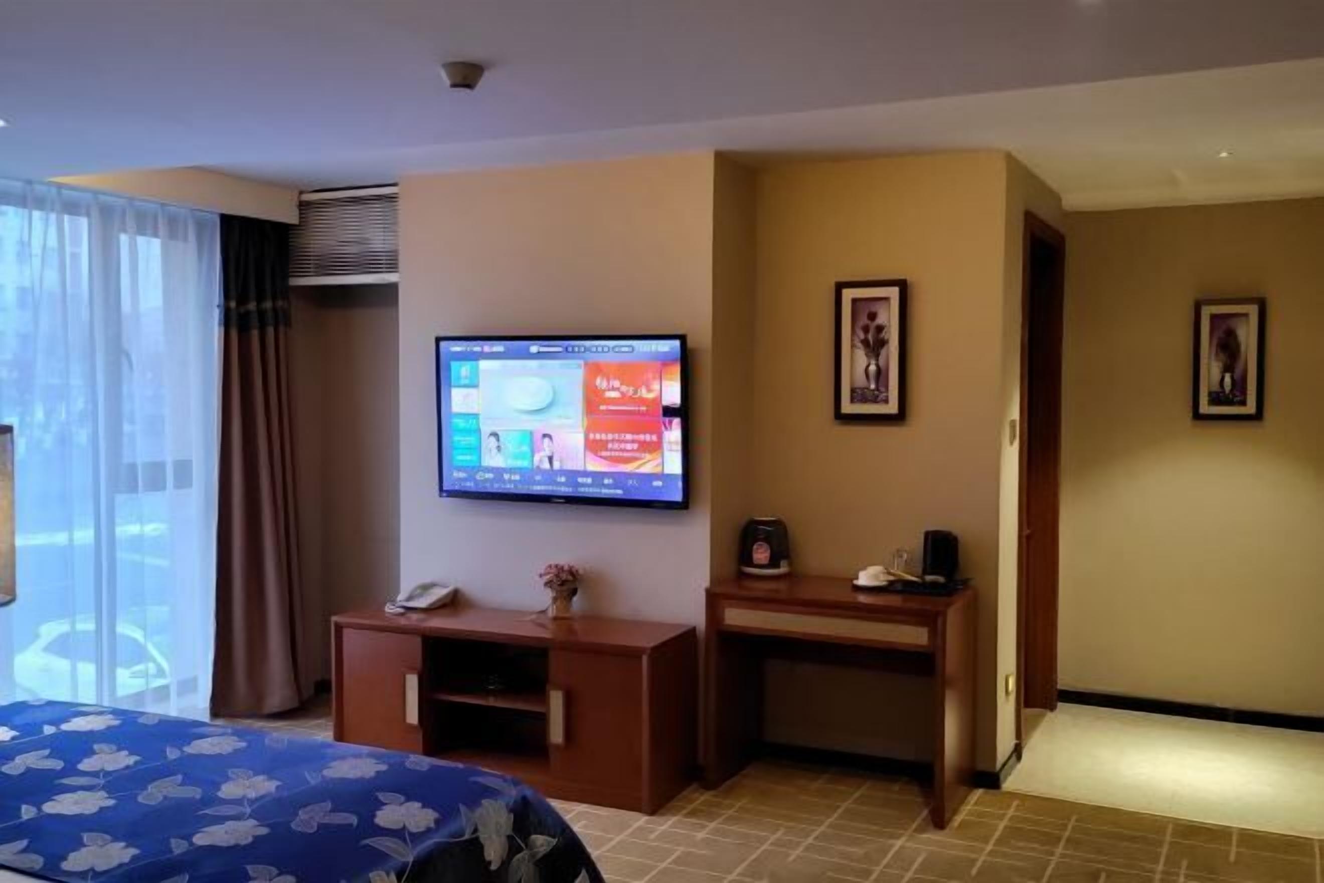 Habitación de hotel con una cama, un televisor en la pared, un escritorio y un mueble bajo.