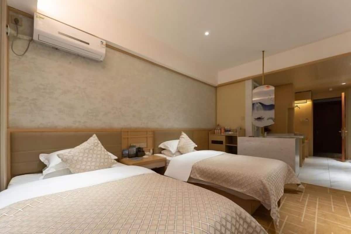 A hotel room with two beds, a bedside table with a lamp, a mirror, and an air conditioning unit.