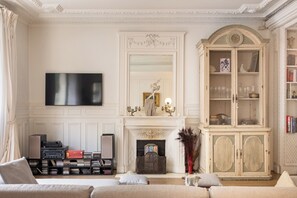 A living room with a fireplace, a television mounted on the wall, a bookshelf, and a cabinet with glassware. - Fabulous 4BD Apartment 5 mins to the Eiffel Tower (Paris)
