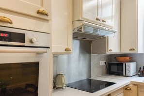 A kitchen with white cabinets, a microwave, a kettle, and a digital clock displaying 15:12. - Fabulous 4BD Apartment 5 mins to the Eiffel Tower (Paris)