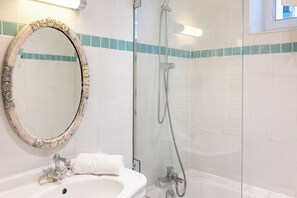 A bathroom with a white sink, a mirror with a decorative frame, a shower with a glass door, and a window above the shower.