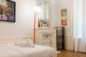 Une chambre d’hôtel avec un lit, une cheminée, un miroir et des œuvres d’art accrochées aux murs.