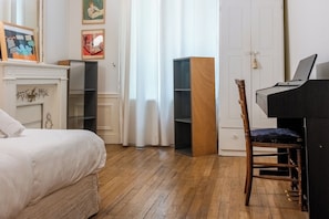A bedroom with a bed, a wooden chair, a piano, and a wardrobe.