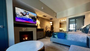Un salon moderne avec un téléviseur à écran plat fixé au-dessus d’une cheminée, un canapé, une petite table ronde et un coin cuisine à l’arrière-plan.