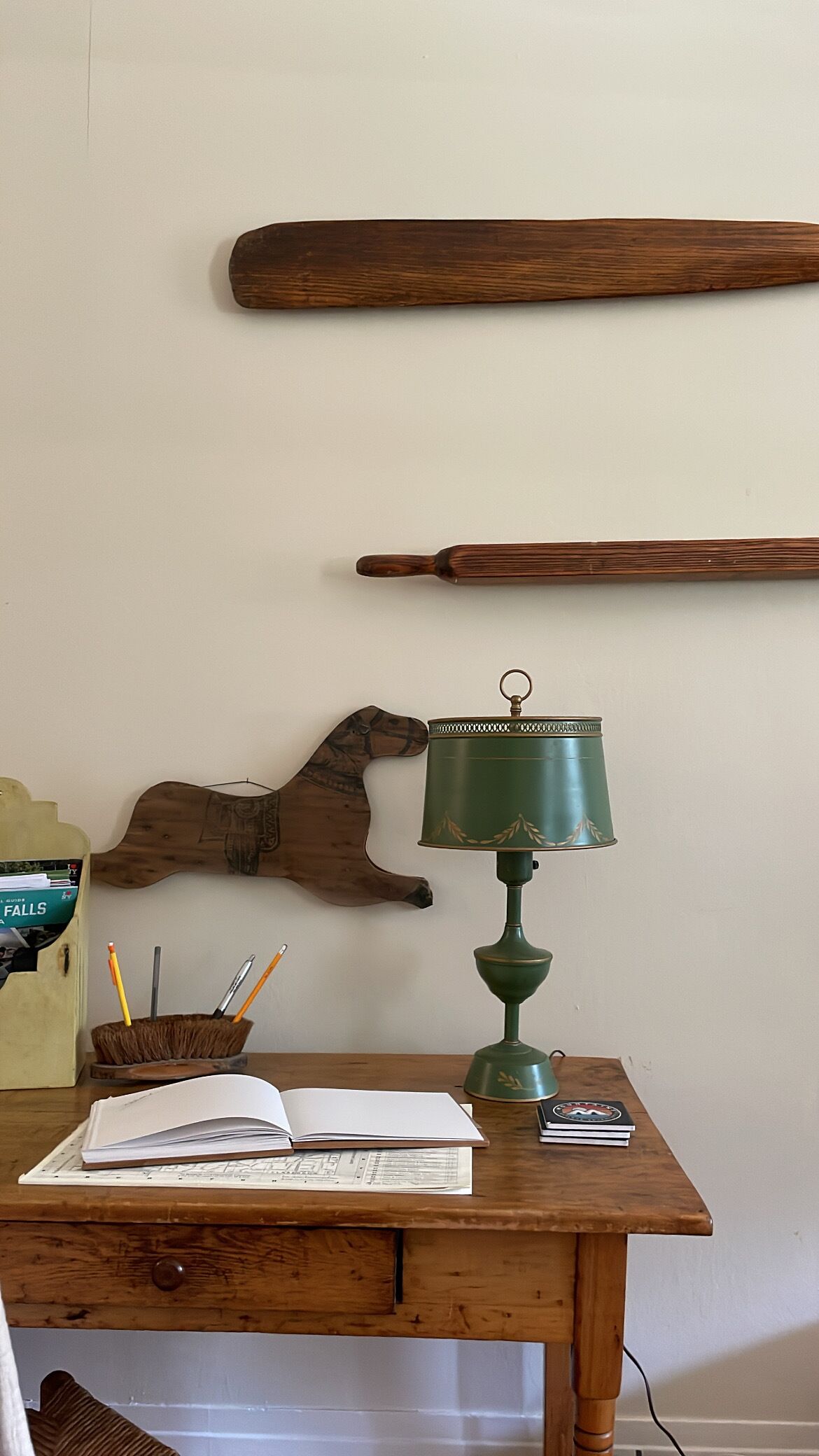 A wooden desk with a green lamp, a book, and a wooden wall decoration.