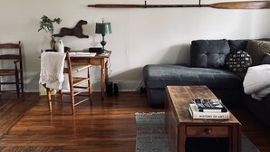 Ein gemütliches Wohnzimmer mit Holzboden, einer grauen Couch, einem Holztisch und einem an der Wand befestigten Schläger.