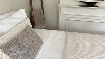 A bedroom with a bed, pillows, a wooden chair, and a sailboat model on a shelf.