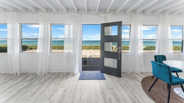 Una habitación con ventanas amplias, una puerta que da al exterior, una mesa blanca y sillas color turquesa.