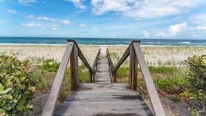 Un paseo marítimo de madera que lleva a la playa, con vista despejada al océano.