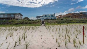 Una playa arenosa con un camino que lleva a un edificio con balcón.