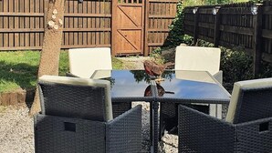 An outdoor patio with a table and four chairs, surrounded by gravel, a wooden fence, and a tree. - Green Cottage (Bangor)