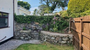 A stone wall garden with plants and flowers, a wooden fence, and a house in the background. - Green Cottage (Bangor)