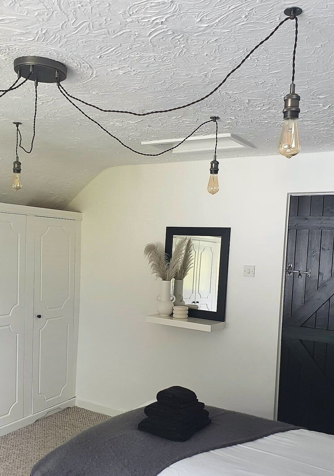 A bedroom with a bed, a bedside table, a mirror, and a door.