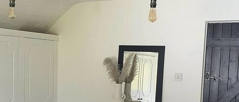 A bedroom with a bed, a bedside table, a mirror, and a door.